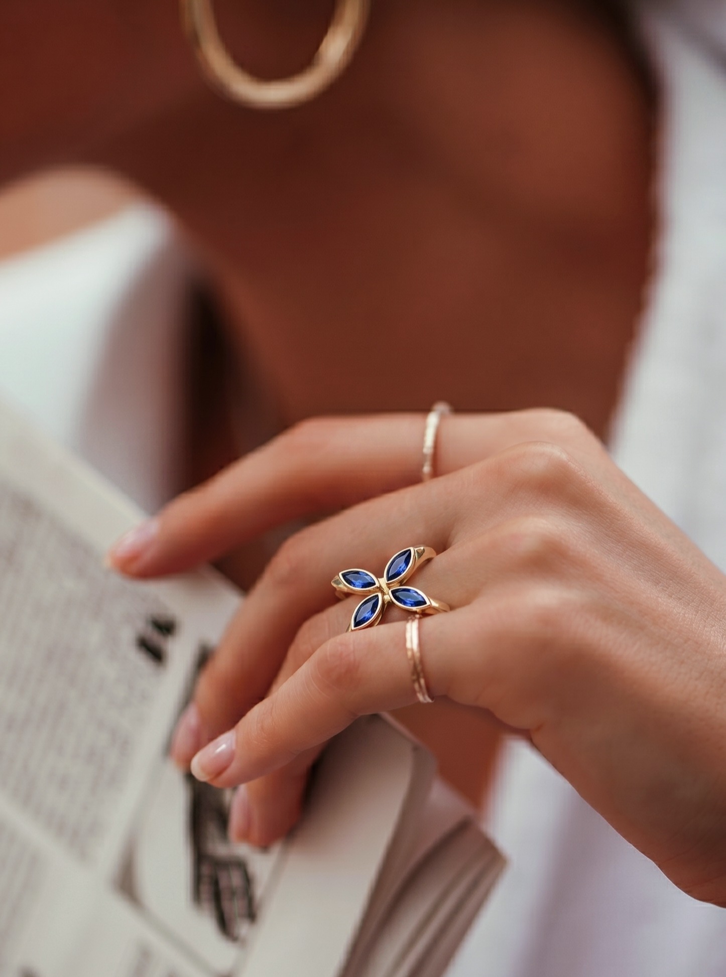 A hand wearing the Quatrefoil Ring resting on the open page of a newspaper, warm morning light.
